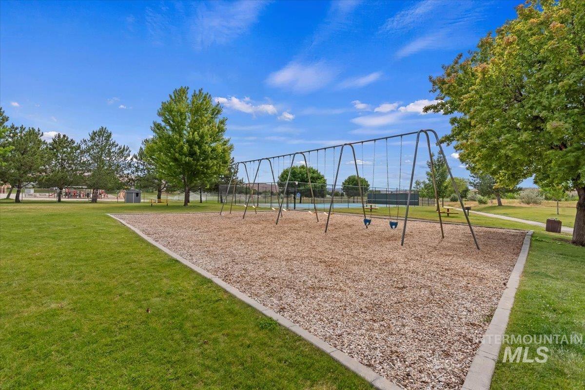 Community park featuring a swing set with wood chip ground covering, surrounded by green lawn and mature trees