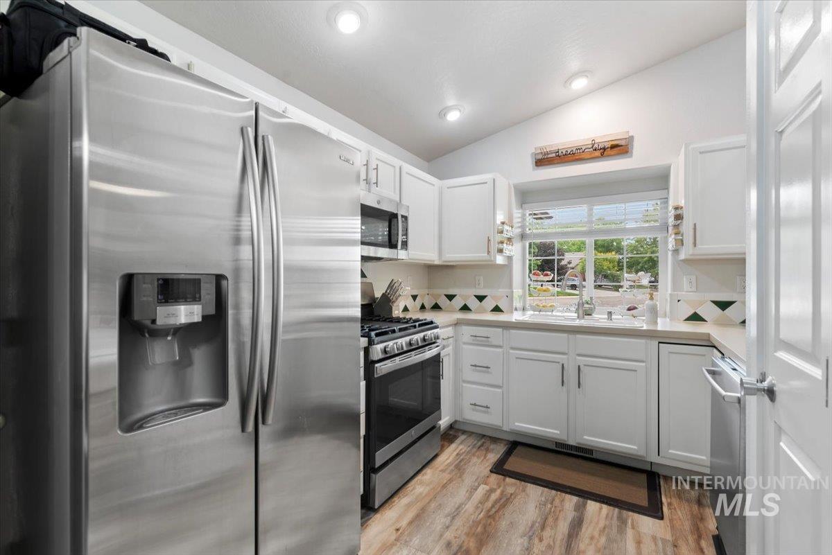 Kitchen featuring white cabinetry, stainless steel appliances, wood-finish flooring, a patterned tile backsplash, and recessed lighting