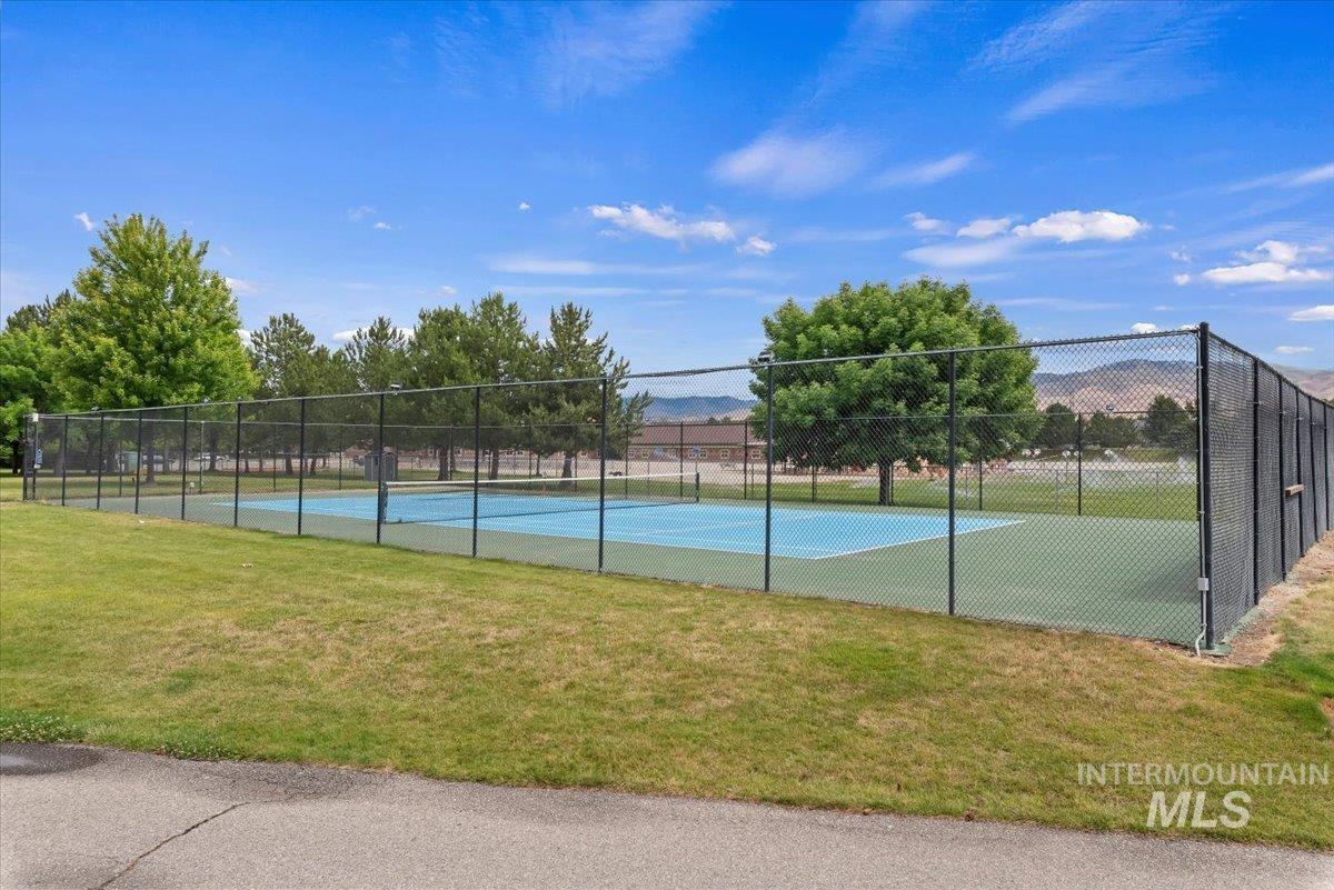 Fenced tennis court featuring a blue playing surface with white lines, surrounded by a green perimeter