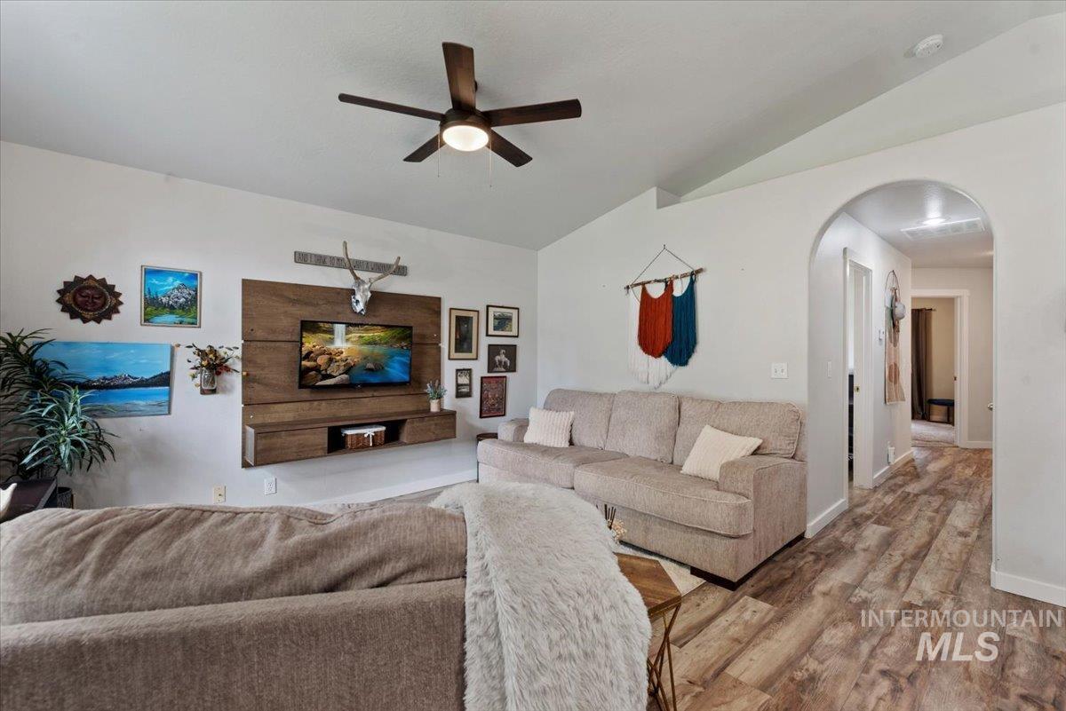 Living area with vaulted ceilings, wood-finish flooring, a contemporary ceiling fan with integrated lighting, a built-in wood media console, and an arched doorway