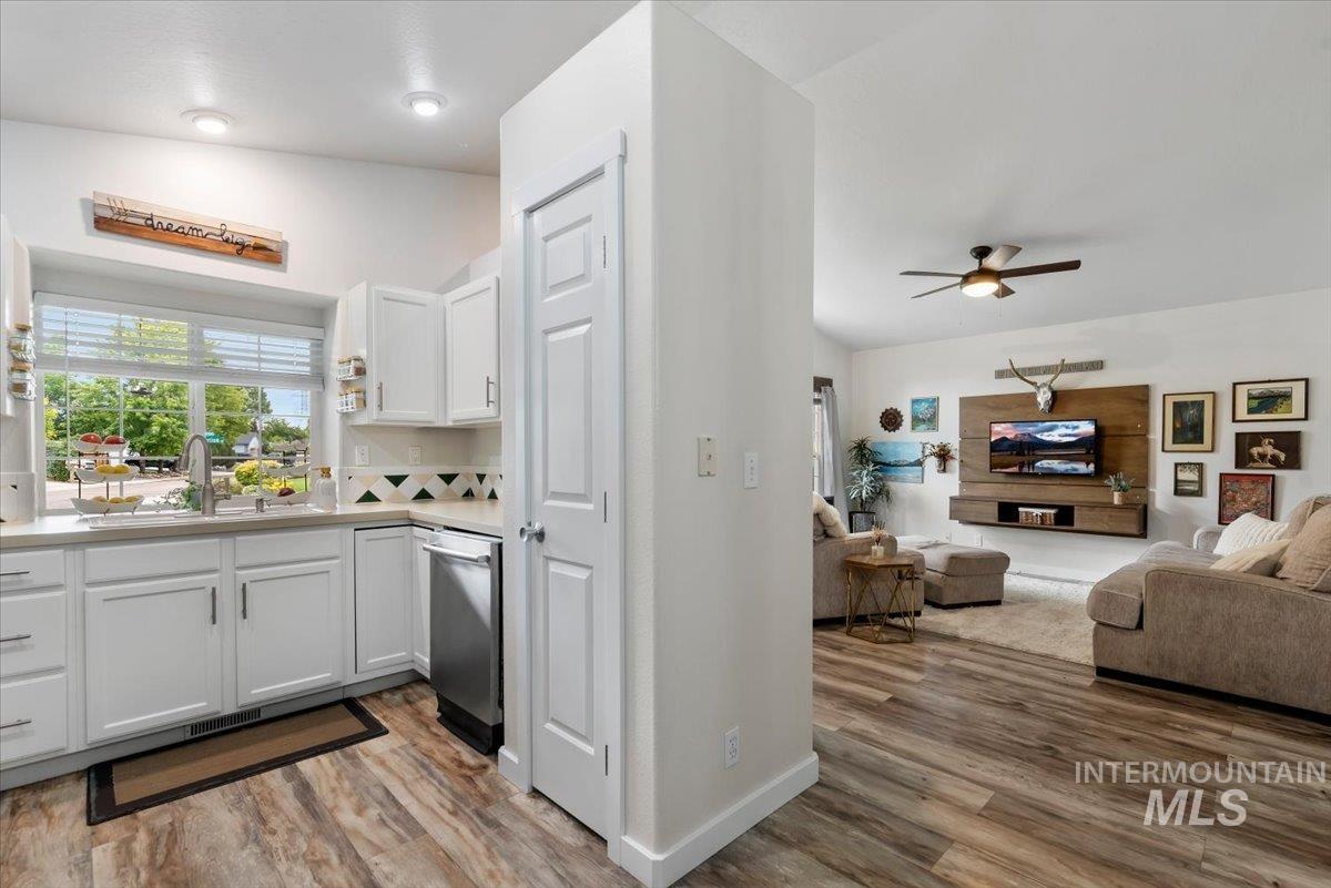 Open-concept living space featuring a kitchen with white cabinetry and a window over the sink, wood-finish flooring, and recessed lighting