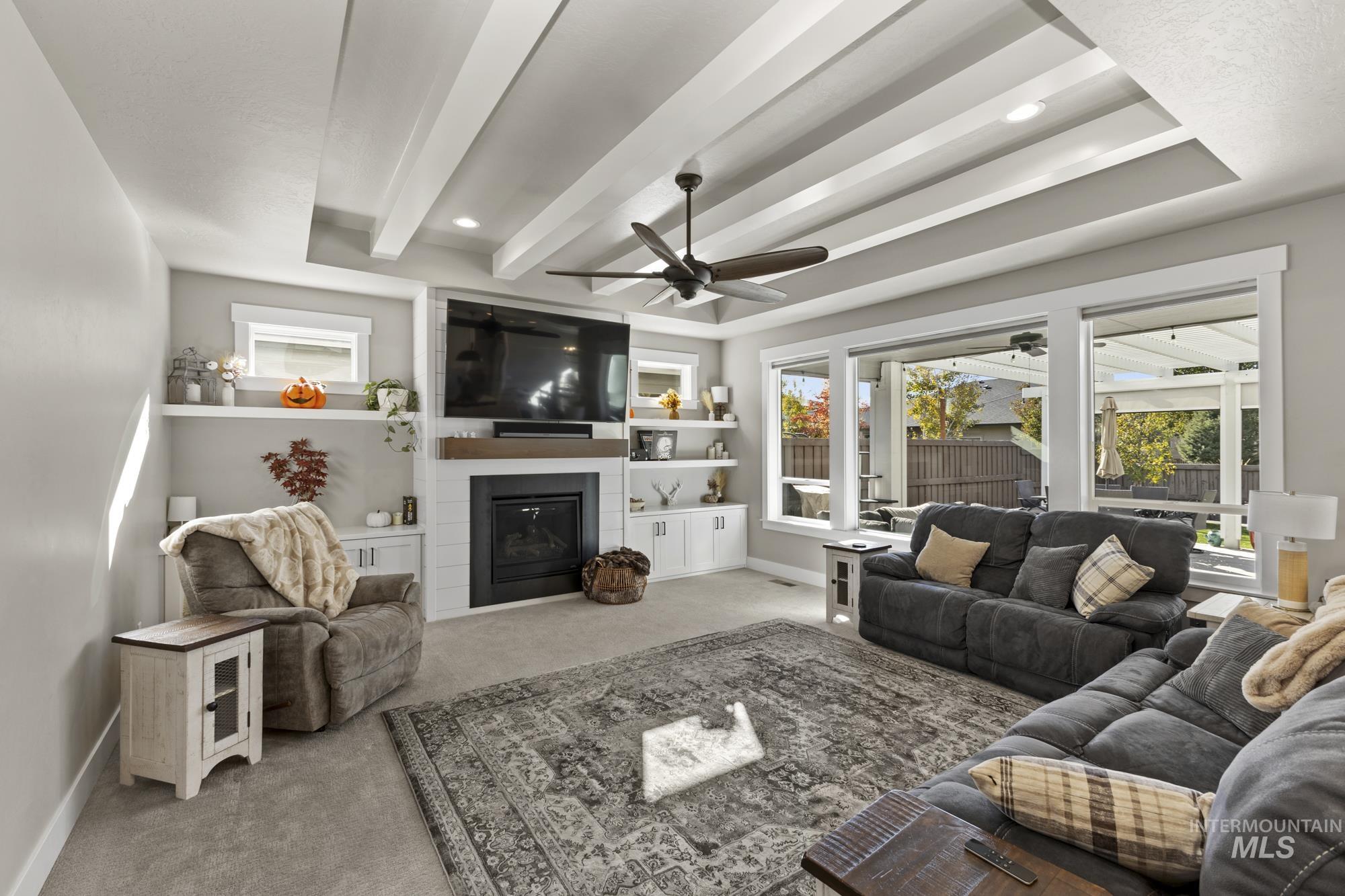 Living room featuring carpet flooring, beam ceiling, a large fireplace, a ceiling fan, and a raised ceiling