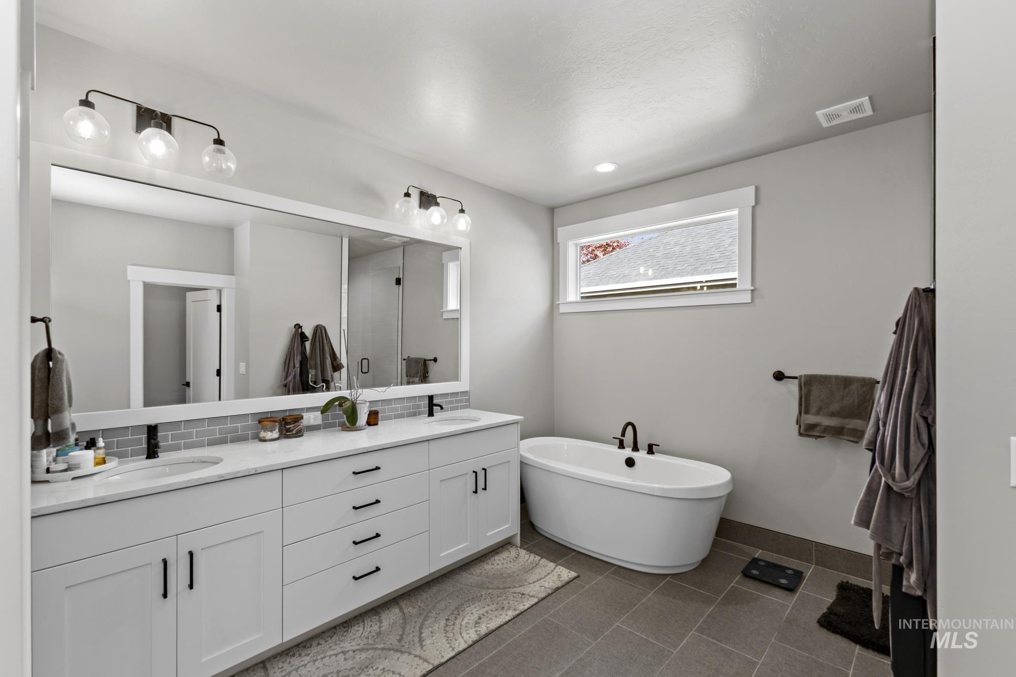 Bathroom with double vanity, a freestanding tub, dark tile patterned floors, and decorative backsplash