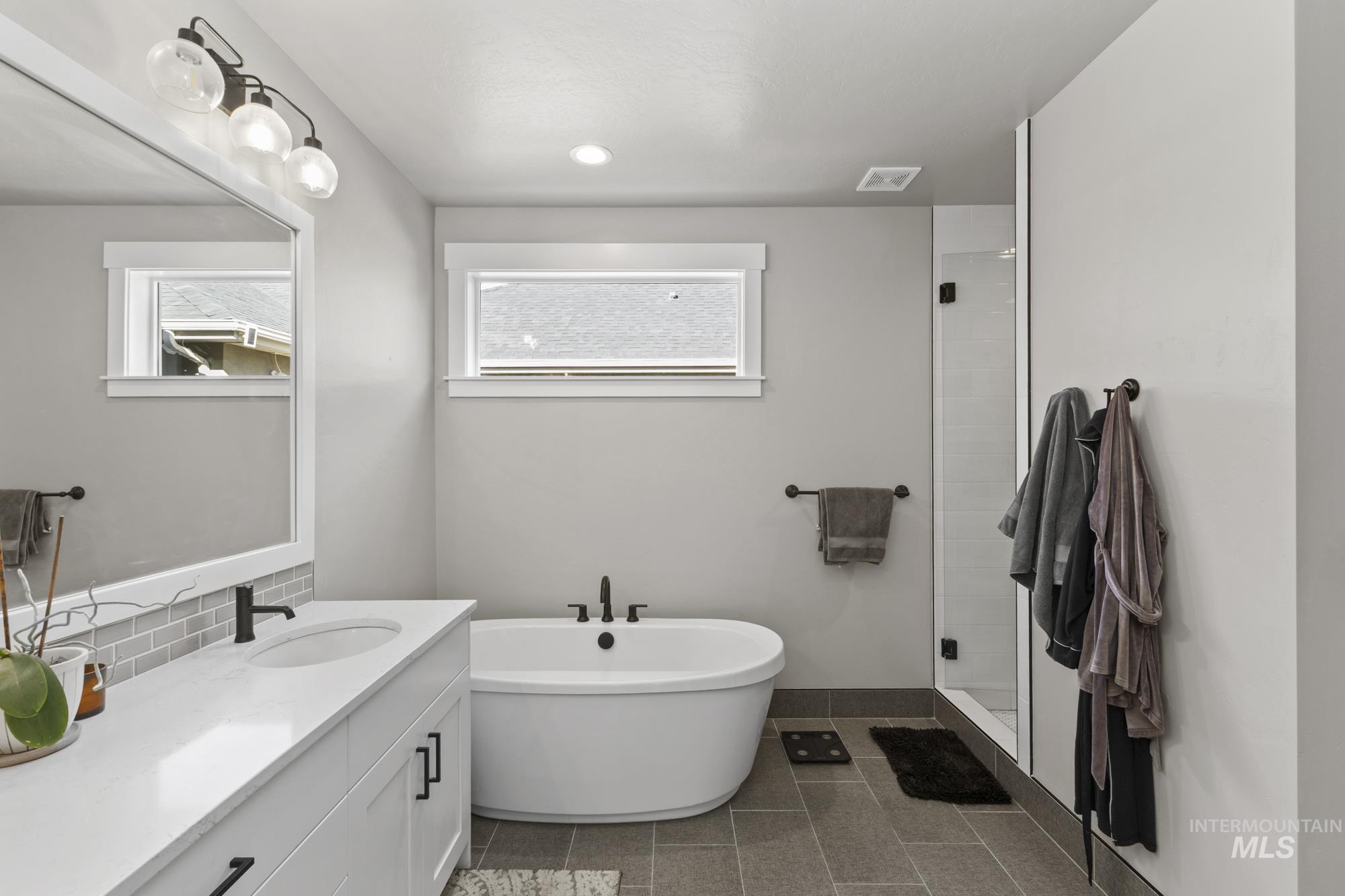 Full bathroom featuring a freestanding bath, vanity, a stall shower, dark tile patterned floors, and backsplash