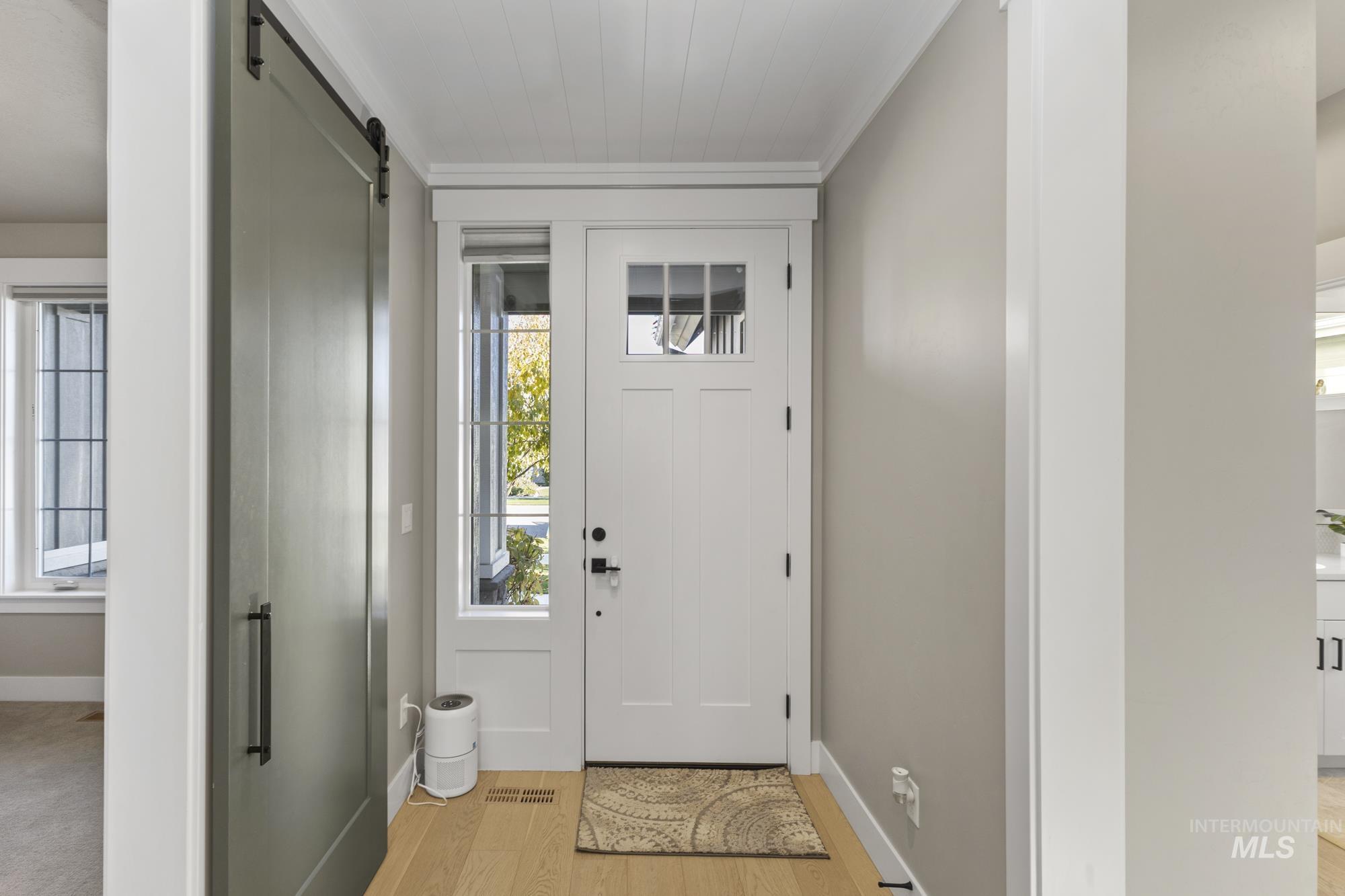Entrance foyer featuring a barn door, light wood finished floors, and crown molding