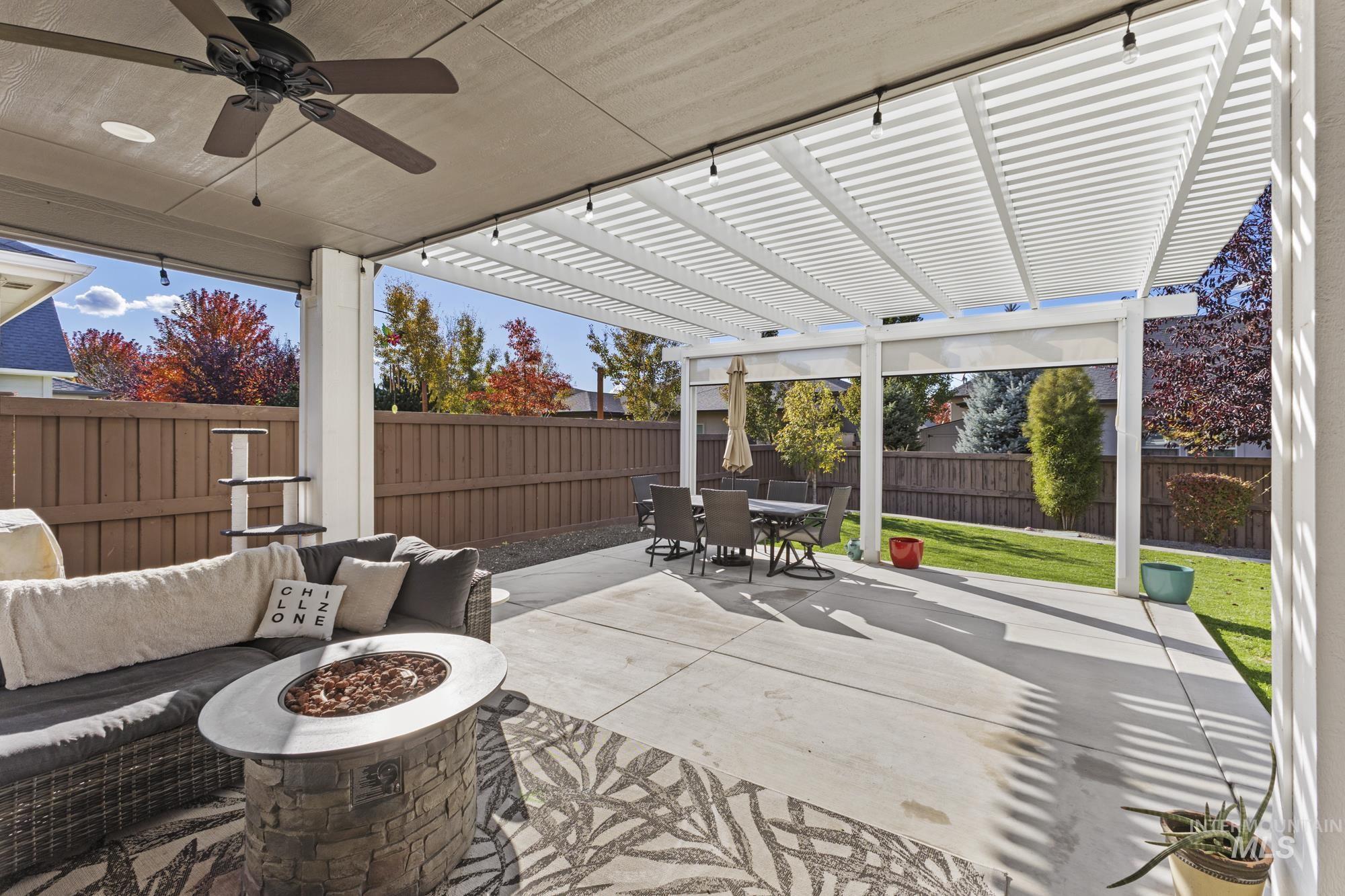 Fenced backyard featuring a pergola, an outdoor living space with a fire pit, a patio area, a ceiling fan, and outdoor dining space