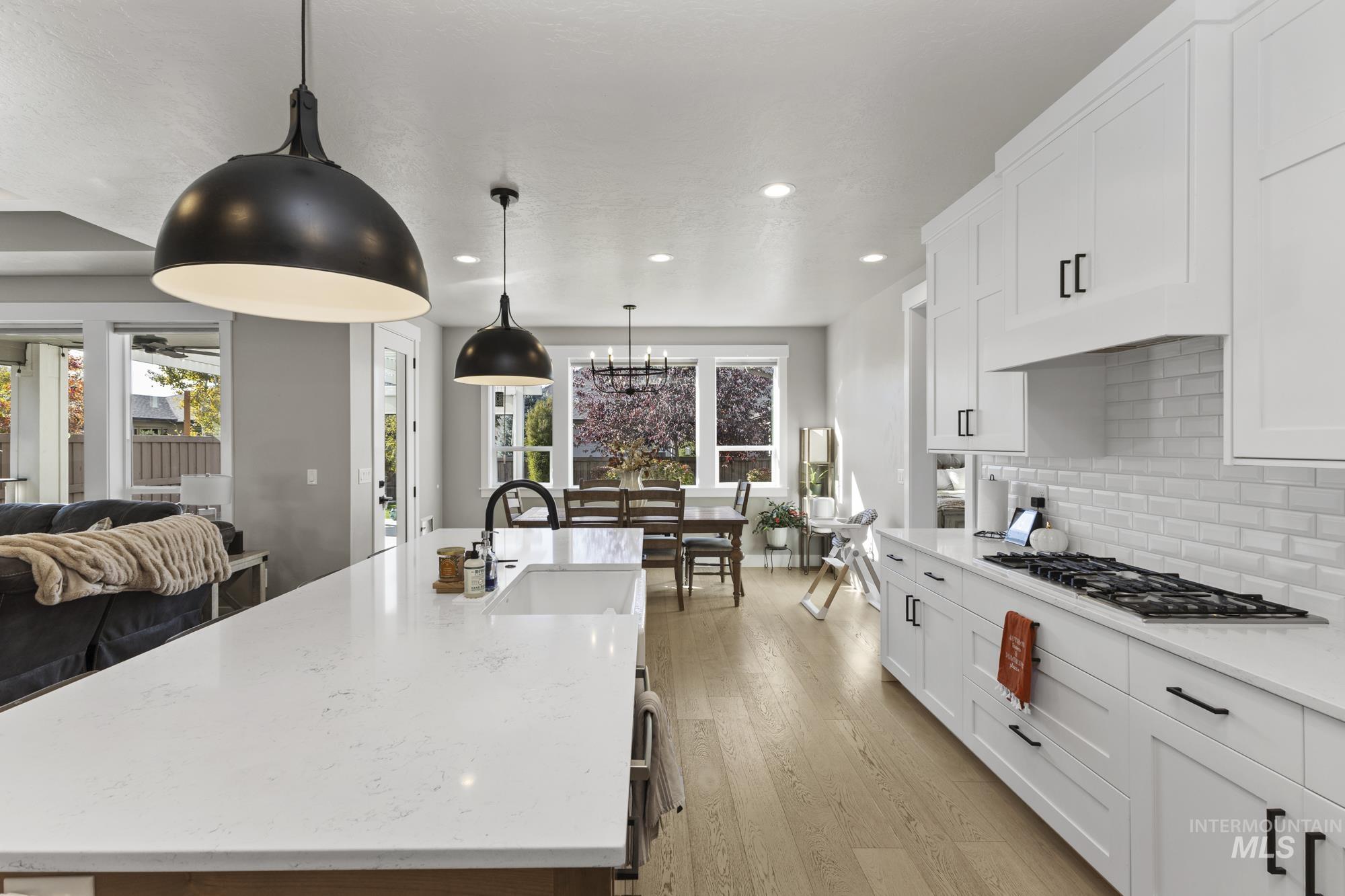 Kitchen with decorative backsplash, open floor plan, white cabinetry, a large island with sink, and light stone counters