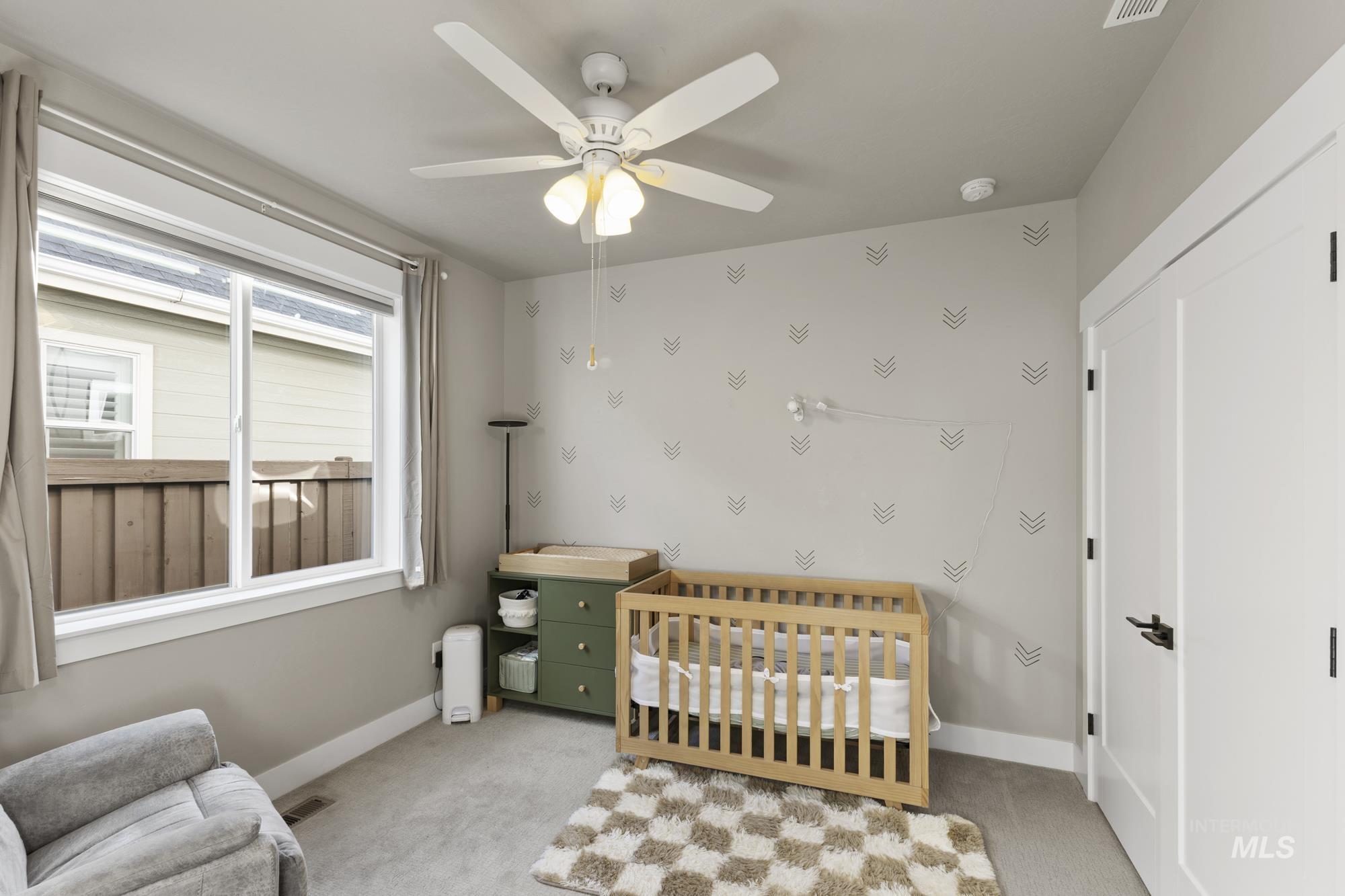 Bedroom featuring a crib, light colored carpet, and ceiling fan