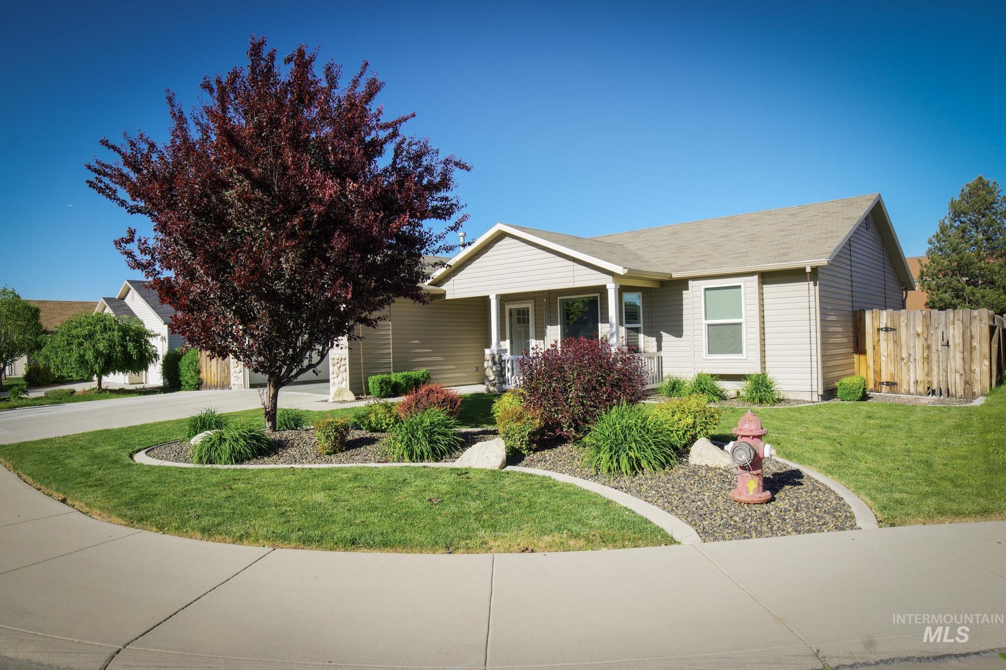Single-story residence featuring light-colored siding, a covered front porch, and a gravel-mulched landscaping bed with a mature deciduous tree