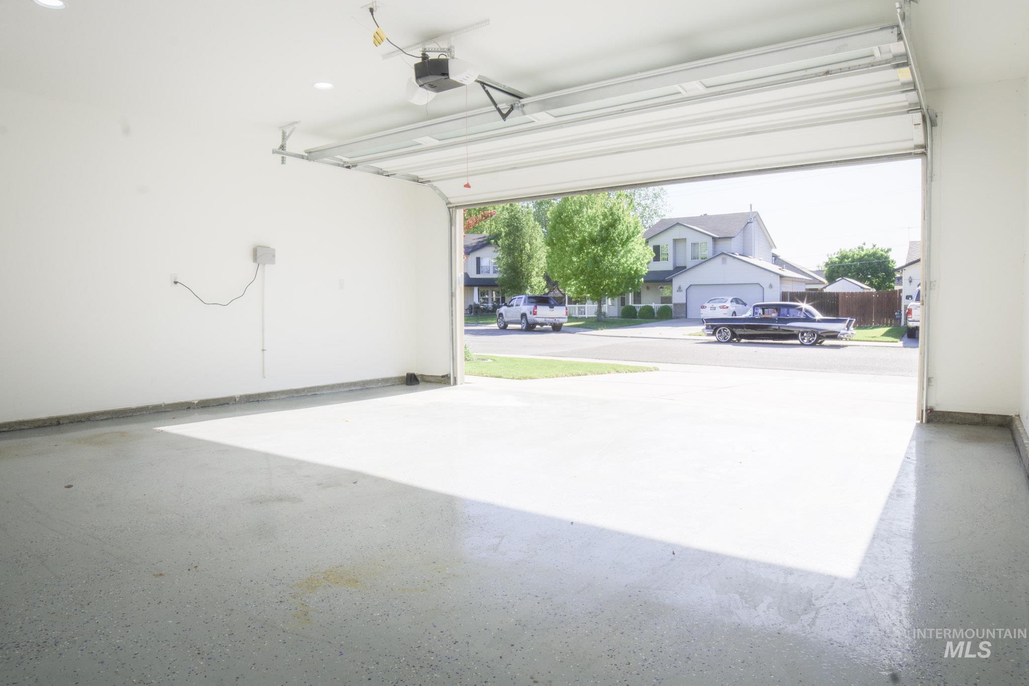 Spacious garage featuring a light-colored, speckled epoxy floor, white painted walls, and an automatic garage door opener