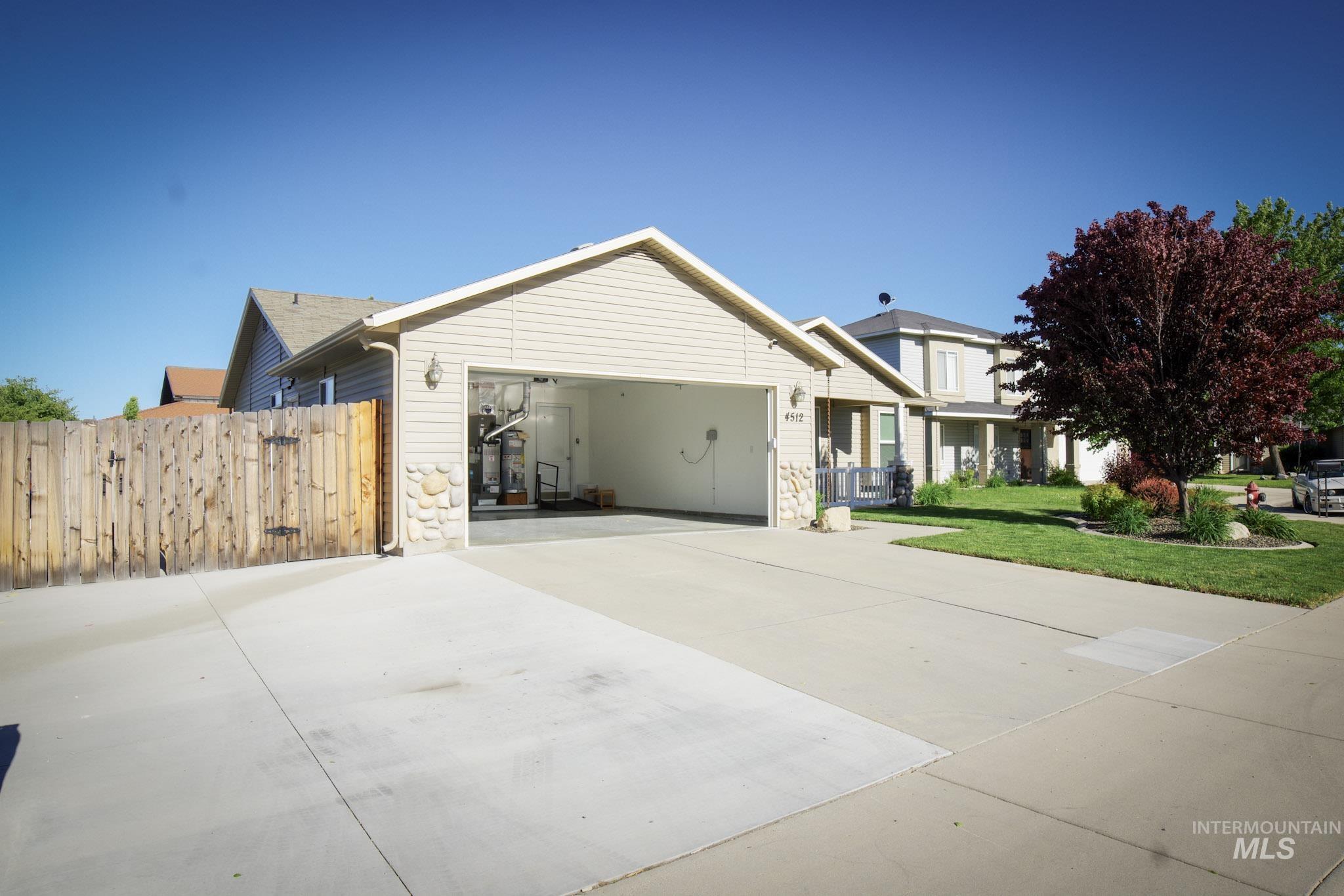 Front exterior featuring a two-car garage with an open bay, light-colored siding, and stone accents