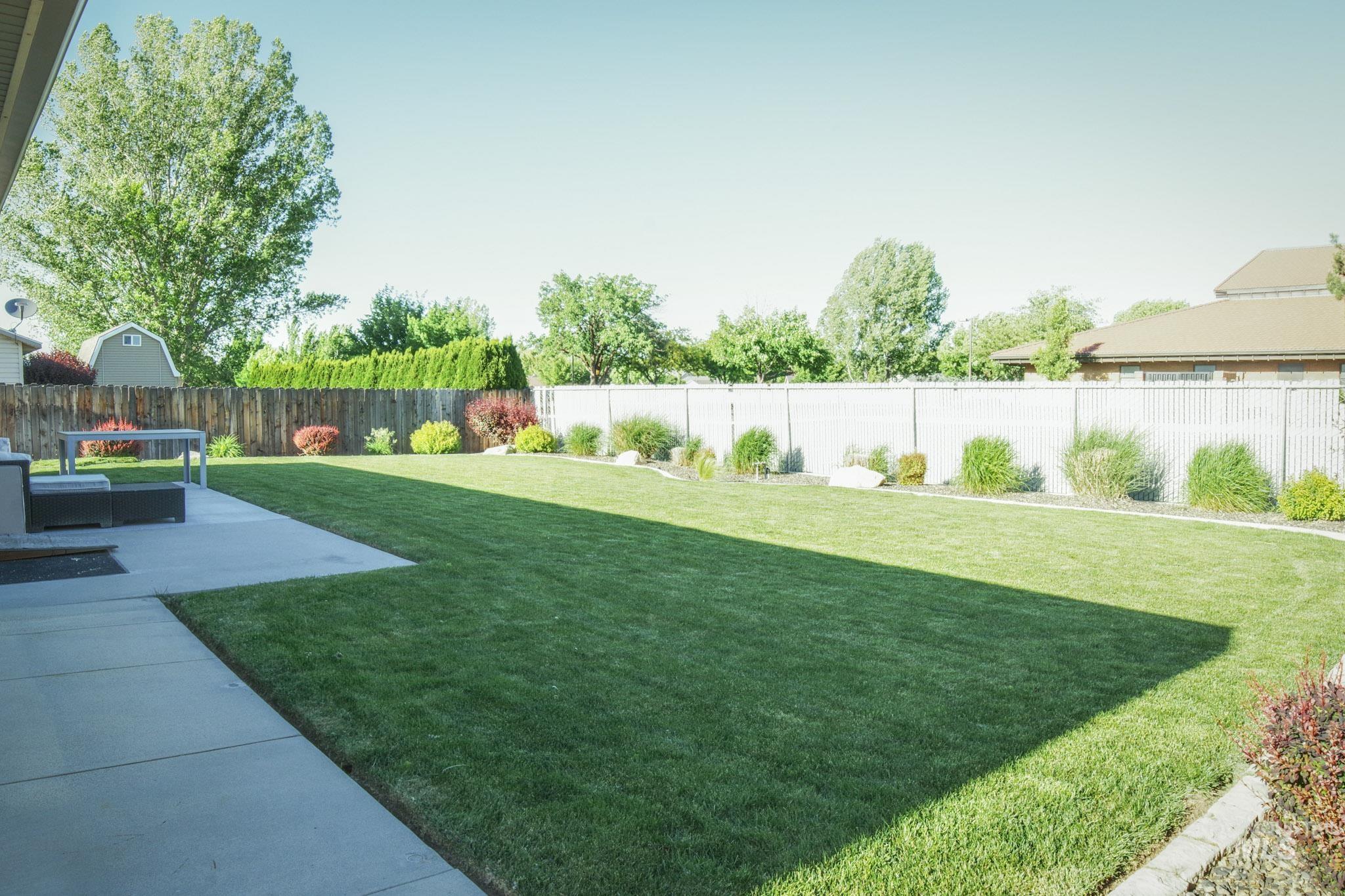 Expansive backyard featuring a lush lawn, concrete patio, perimeter landscaping, and a privacy fence