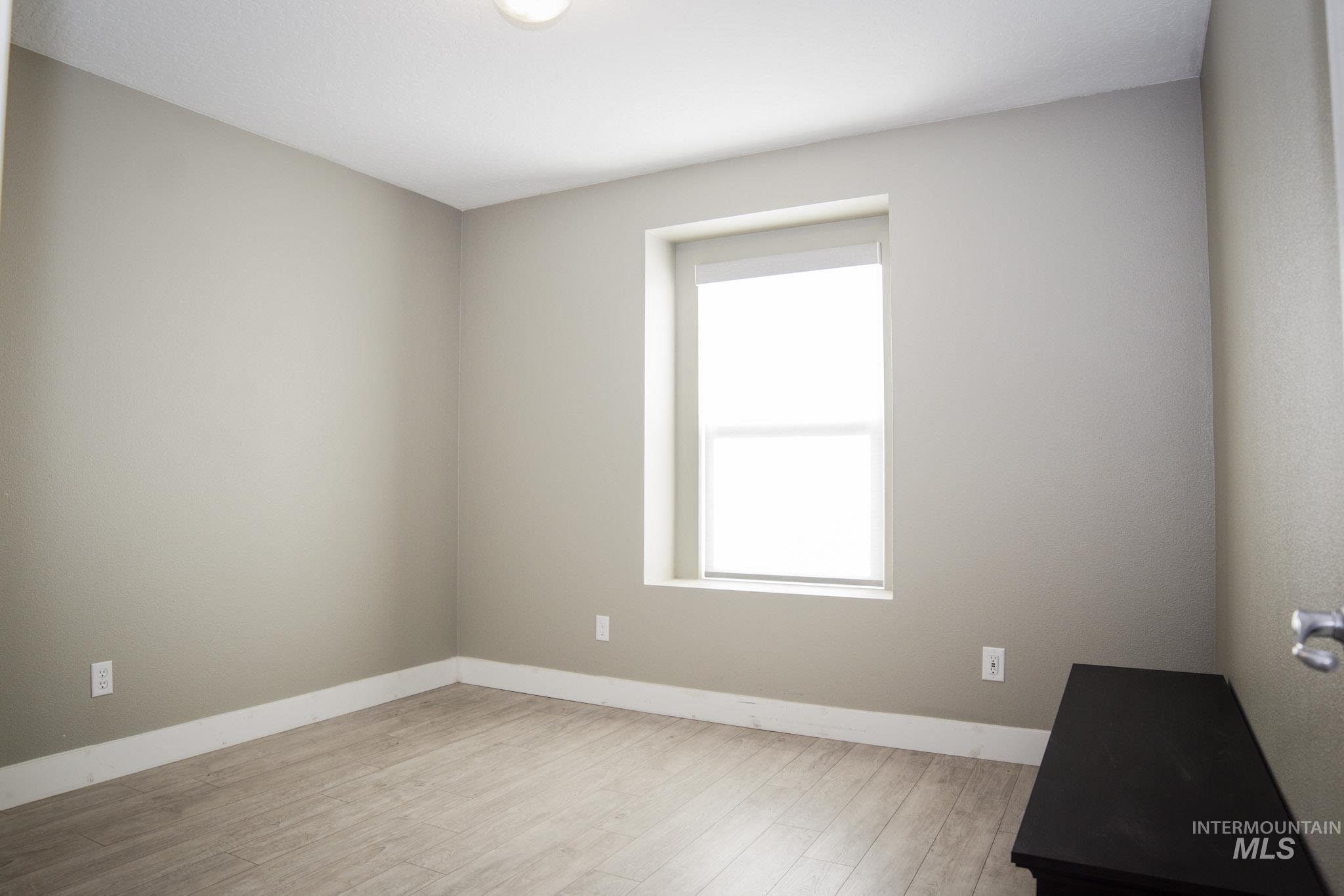 Neutral tone room with wood-finish flooring and a single window with a white roller blind