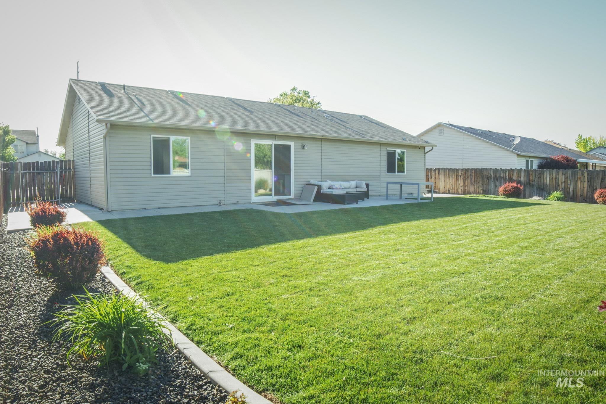Spacious backyard featuring a manicured lawn, concrete patio, and mature landscaping