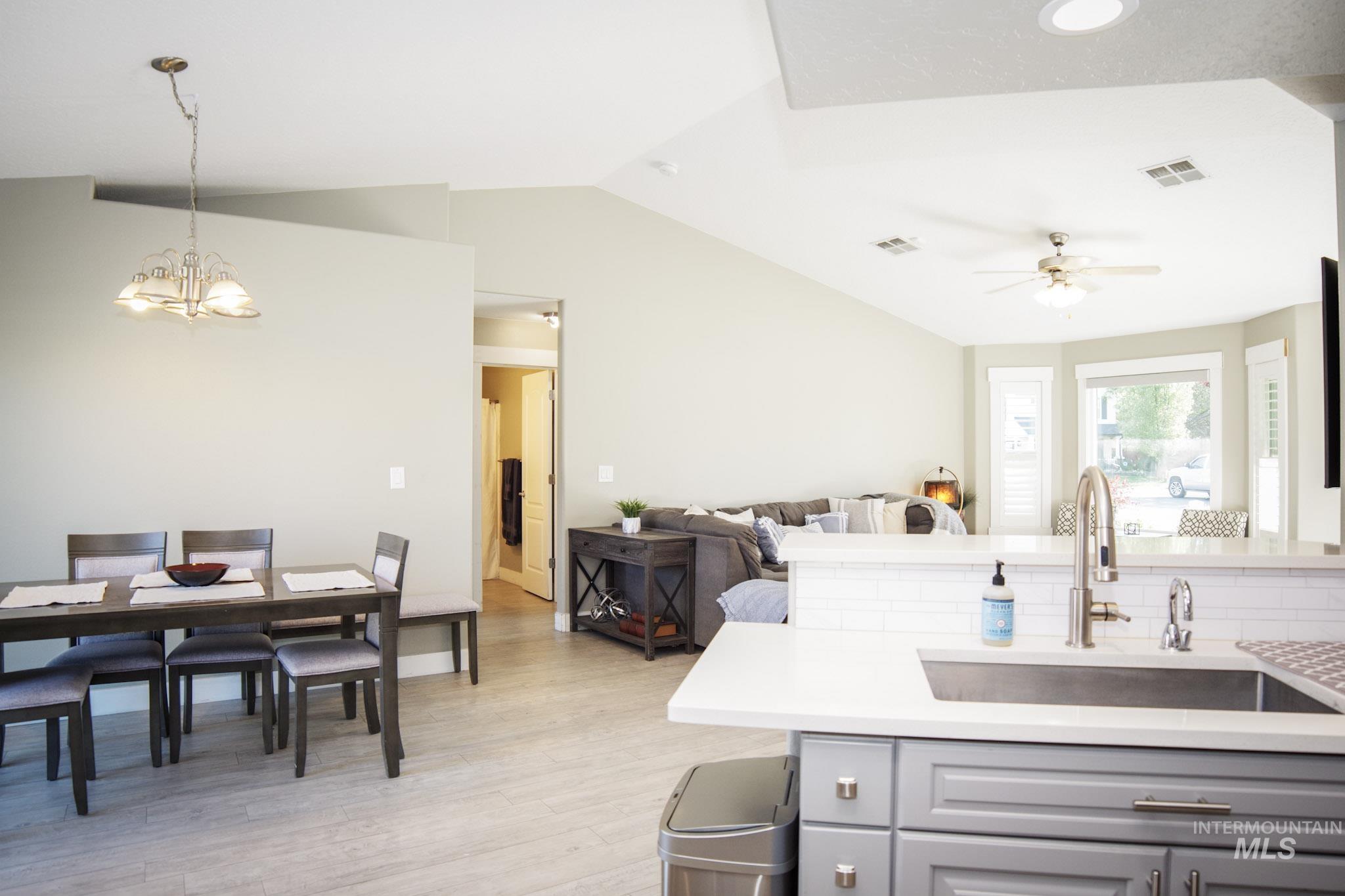 Open-concept living area featuring a kitchen island with built-in sink, vaulted ceilings, light wood-finish flooring, and a dining area with pendant lighting