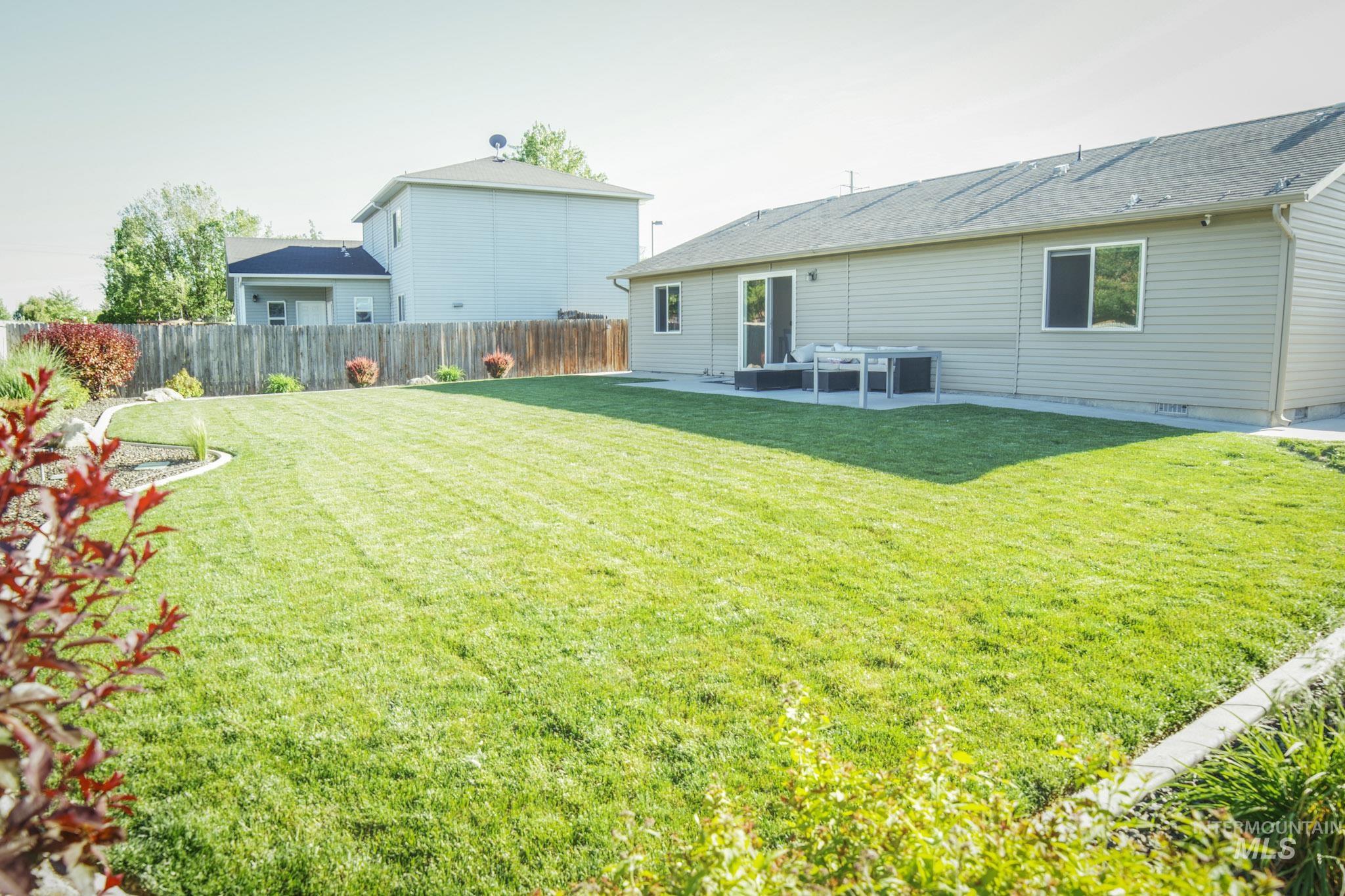 Expansive grass lawn with perimeter landscaping and a wooden privacy fence
