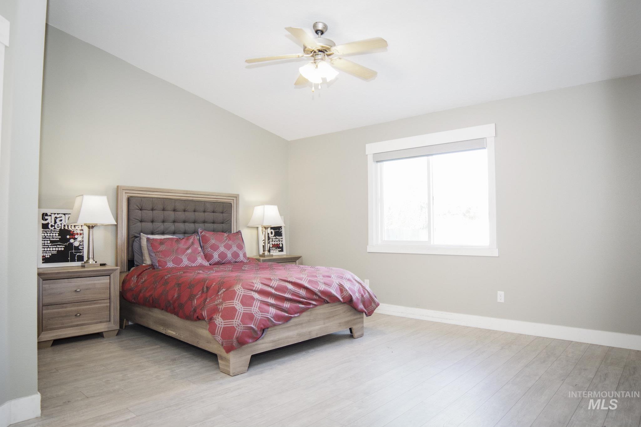 Expansive bedroom featuring vaulted ceilings, wood-finish flooring, a contemporary ceiling fan, a large window, and light neutral wall tones
