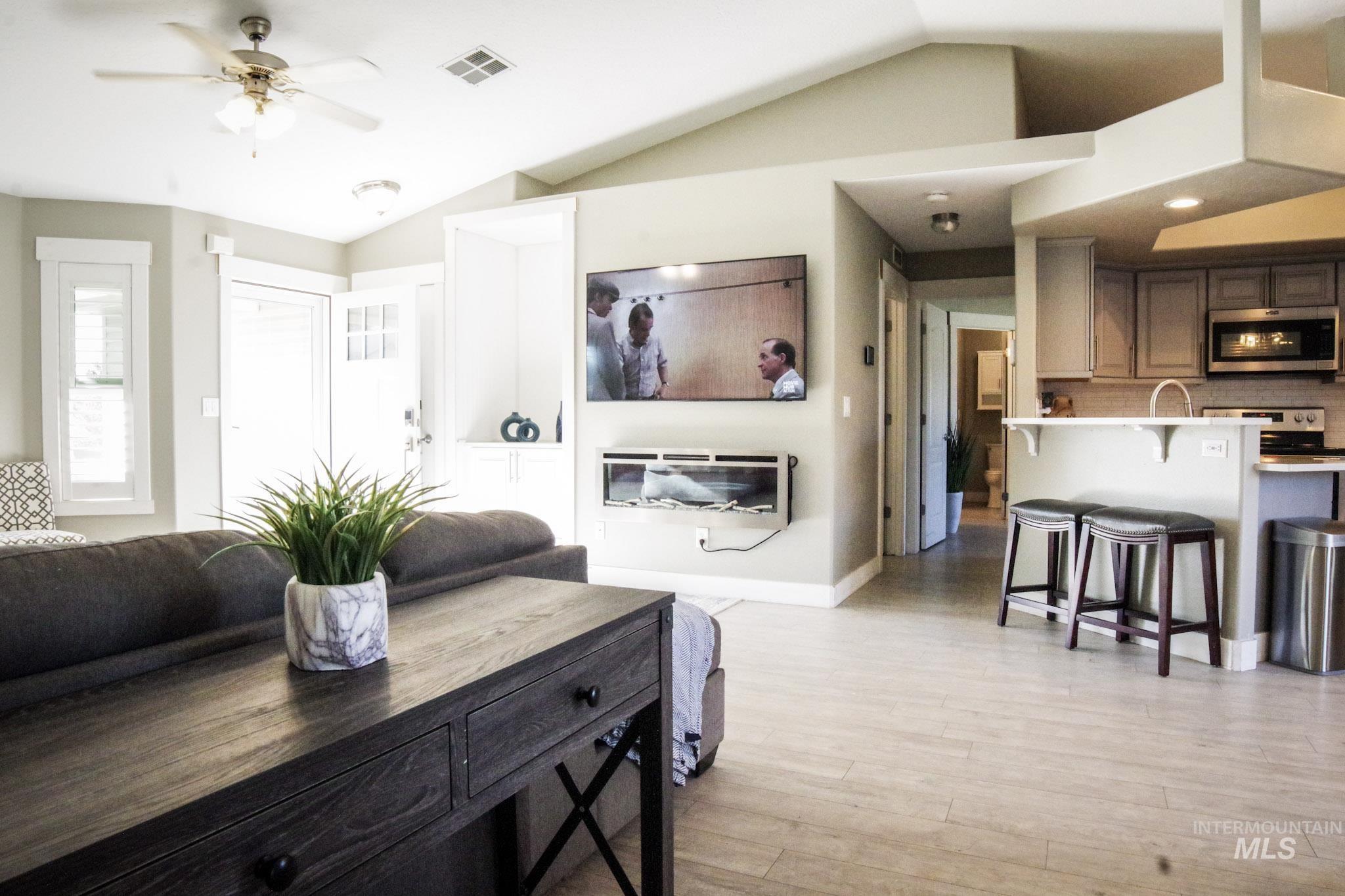 Bright open-concept living space with vaulted ceilings, light wood-finish flooring, built-in shelving, and a modern fireplace feature