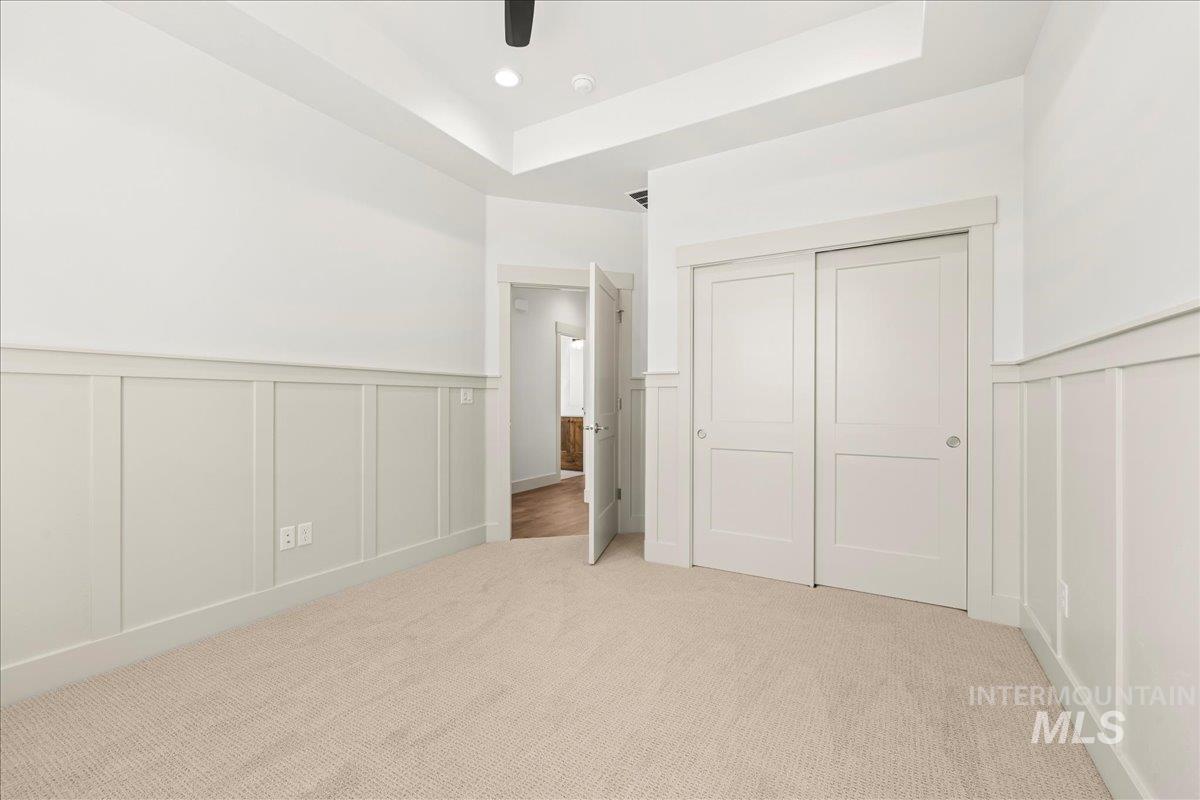 Unfurnished bedroom featuring a decorative wall, a wainscoted wall, a tray ceiling, light carpet, and a closet
