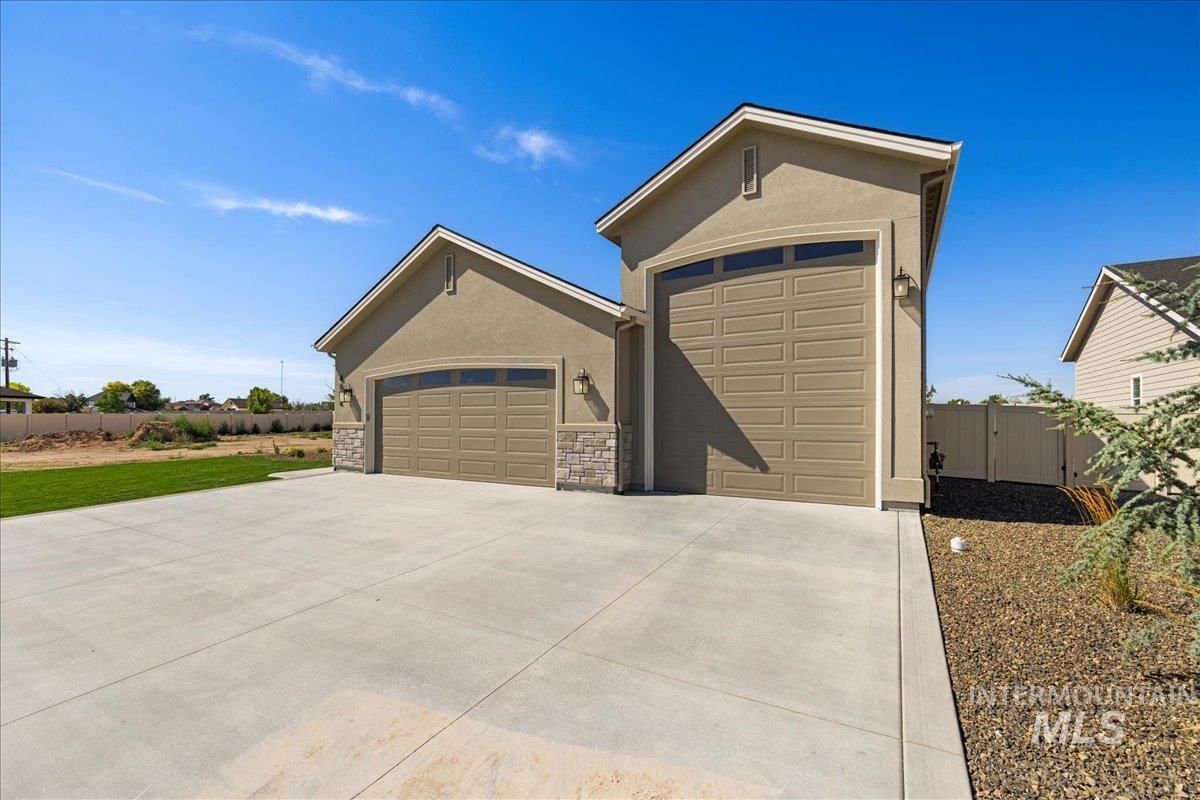Ranch-style home with an attached garage, stucco siding, concrete driveway, stone siding, and a gate