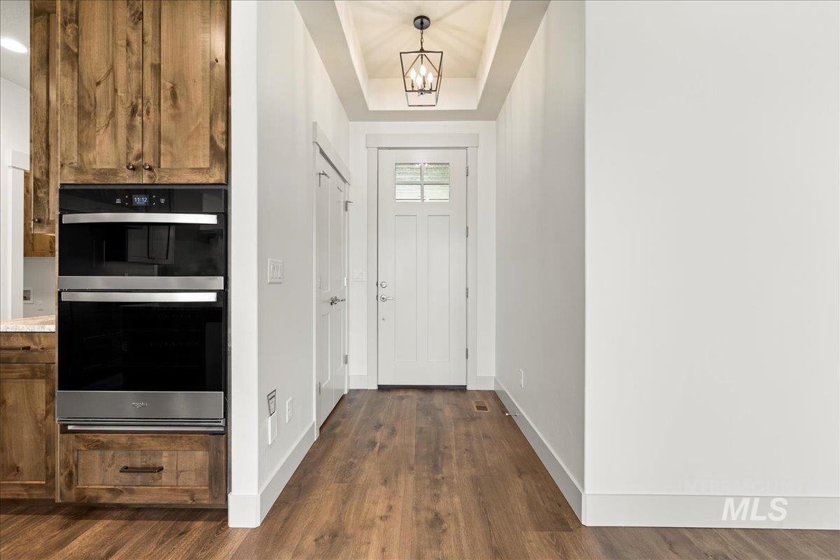 Entryway with a tray ceiling, a chandelier, and dark wood-style flooring