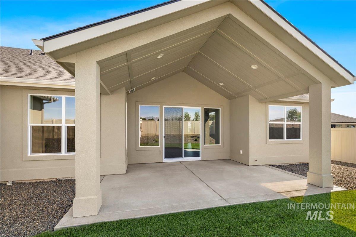 Rear view of house featuring a shingled roof, stucco siding, and a patio