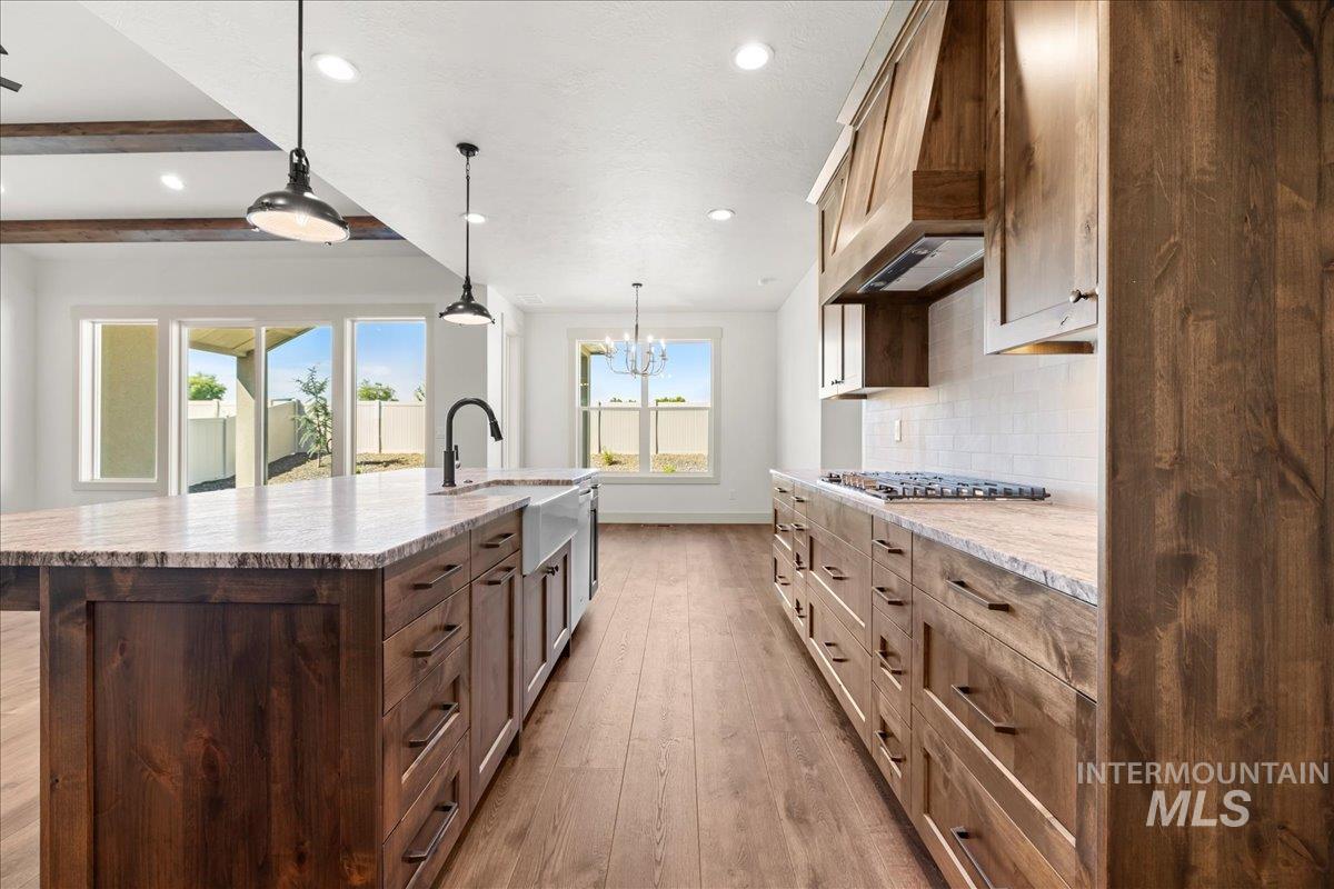 Kitchen with hardwood / wood-style floors, recessed lighting, premium range hood, beam ceiling, and a chandelier