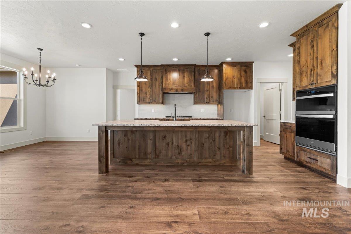 Kitchen with recessed lighting, dark wood finished floors, a chandelier, an island with sink, and decorative light fixtures