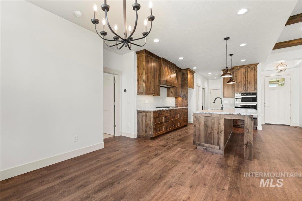 Kitchen featuring a chandelier, dark wood-style flooring, a kitchen island with sink, a kitchen bar, and light stone counters