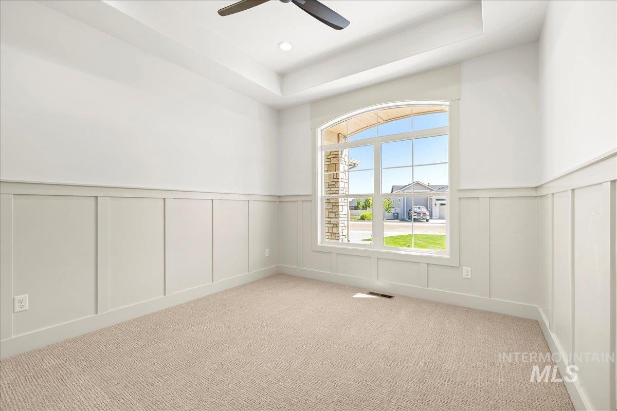 Unfurnished room with a decorative wall, wainscoting, carpet, a ceiling fan, and a tray ceiling