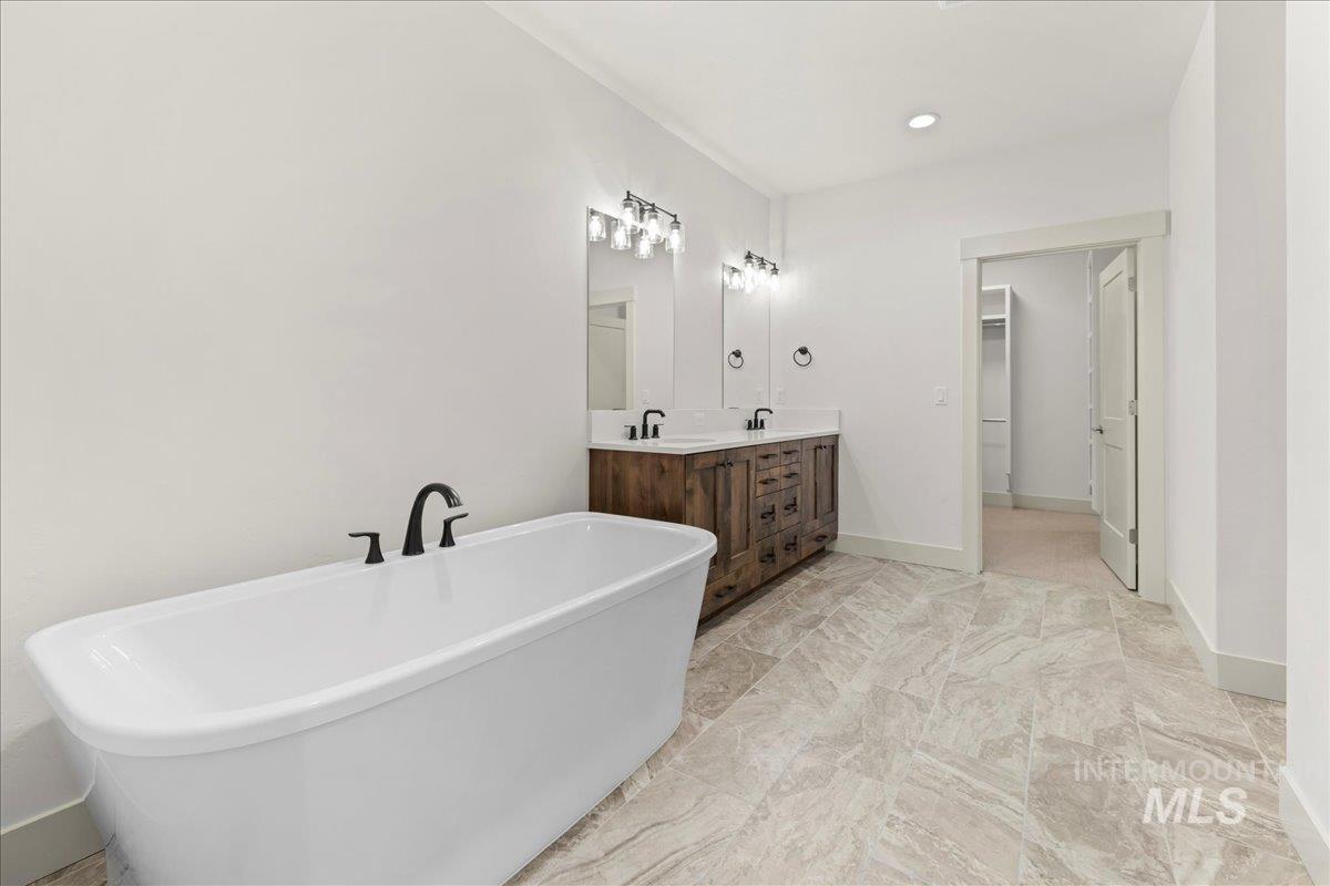 Bathroom with a freestanding tub, double vanity, recessed lighting, and marble finish floors