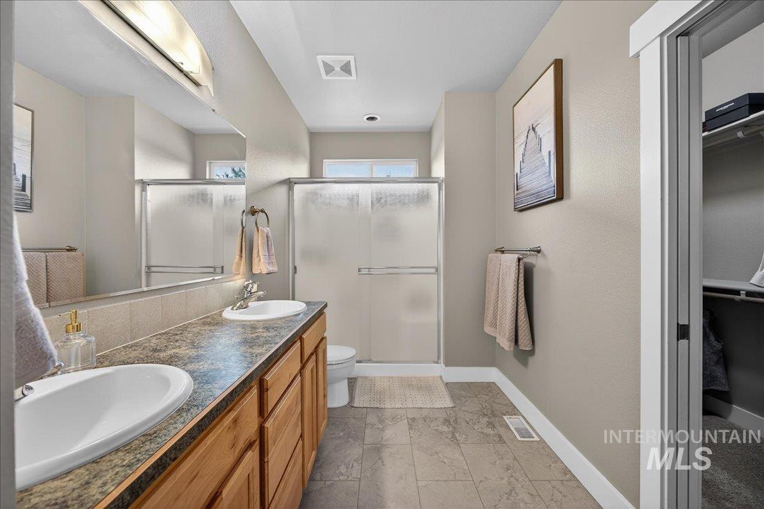 Upstairs primary bathroom featuring a stall shower, a spacious walk-in closet, double vanity, and light finish tile floors.