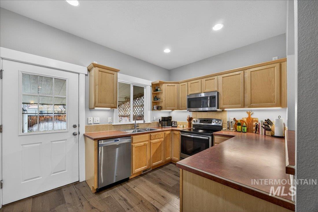 Kitchen featuring stainless steel appliances, open shelves, dark wood finished floors, light wood finish cabinetry, and dark countertops