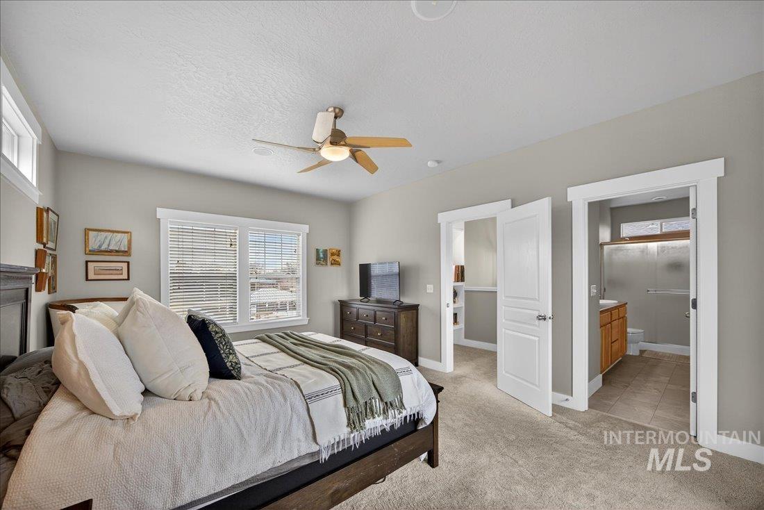 Bedroom with light colored carpet, ceiling fan, ensuite bathroom, and a textured ceiling