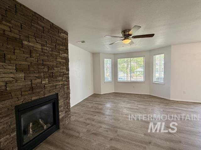 Living space featuring a stone-clad fireplace with a black insert, wood-finish flooring, a ceiling fan with integrated lighting, and bay windows