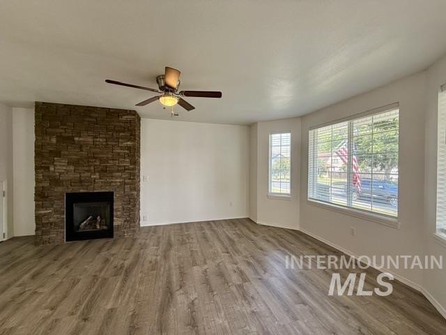 Living area featuring a floor-to-ceiling stacked stone fireplace, wood-finish flooring, a ceiling fan with integrated lighting, and multiple windows with blinds