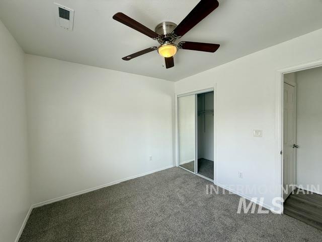 Carpeted room featuring a ceiling fan with light fixture, mirrored sliding closet doors, white baseboards, and a wall-mounted thermostat