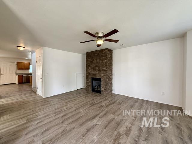 Spacious interior featuring wood-finish flooring, a stacked stone fireplace with an integrated firebox, and a ceiling fan with light fixture