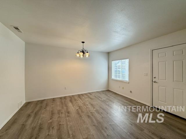 Spacious room featuring wood-finish flooring, a contemporary ceiling light fixture, a window with horizontal blinds, and a paneled entry door