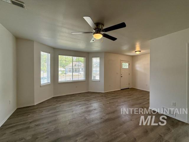 Spacious room featuring wood-finish flooring, a contemporary ceiling fan with integrated lighting, multiple windows with blinds, a white entry door with frosted glass detailing, and recessed lighting