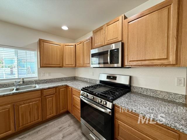 Kitchen featuring wood cabinetry, granite-style countertops, stainless steel appliances, and wood-finish flooring