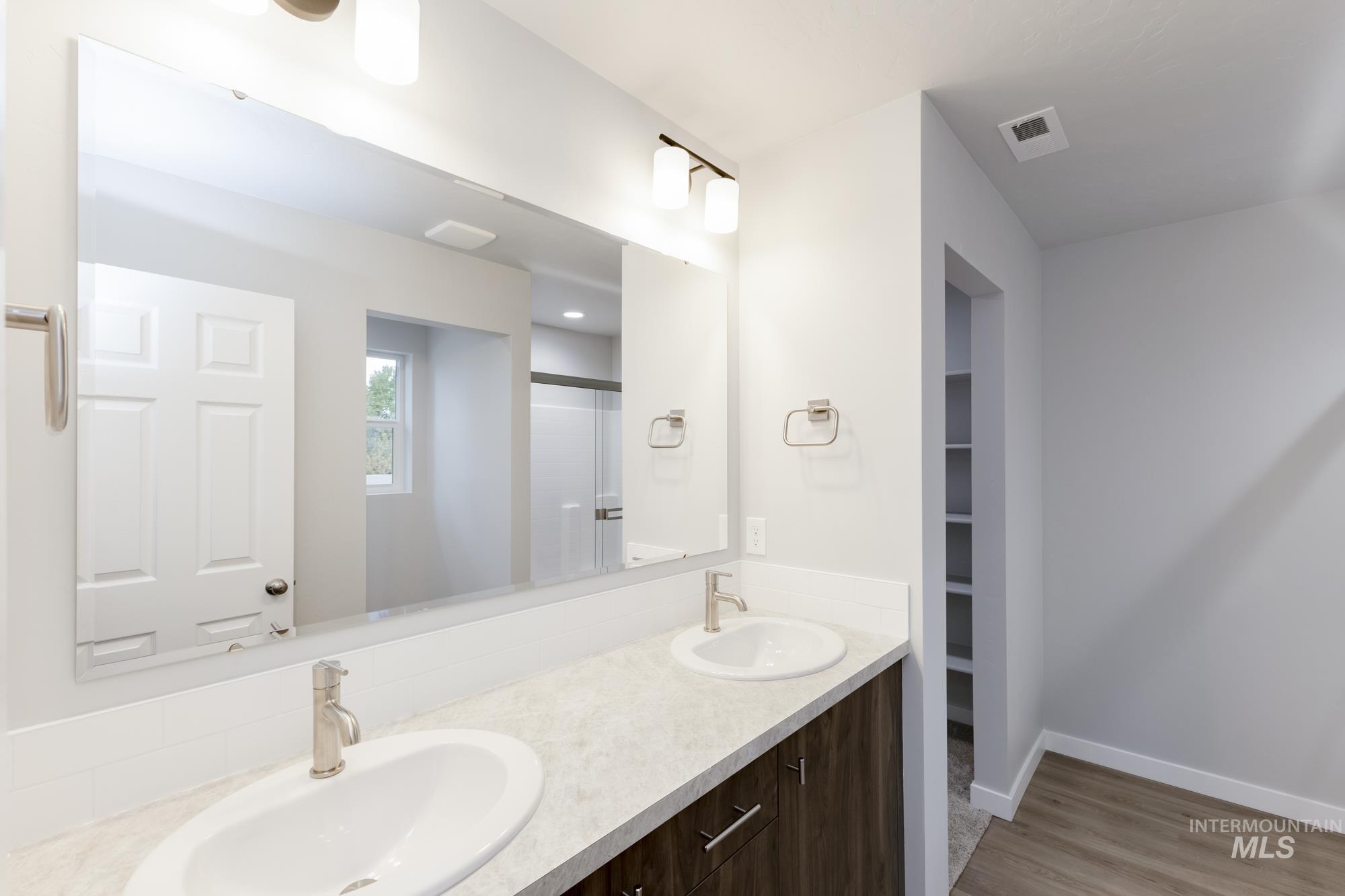 Full bath featuring double vanity, light wood-style flooring, a shower stall, and a walk in closet