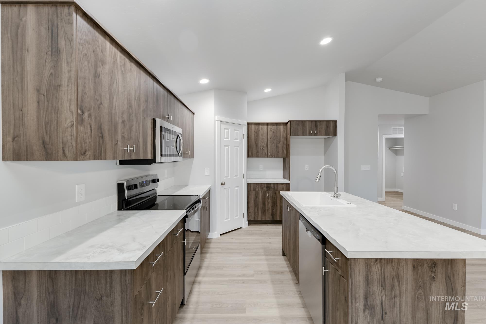 Kitchen featuring stainless steel appliances, modern cabinets, light wood-style flooring, an island with sink, and vaulted ceiling