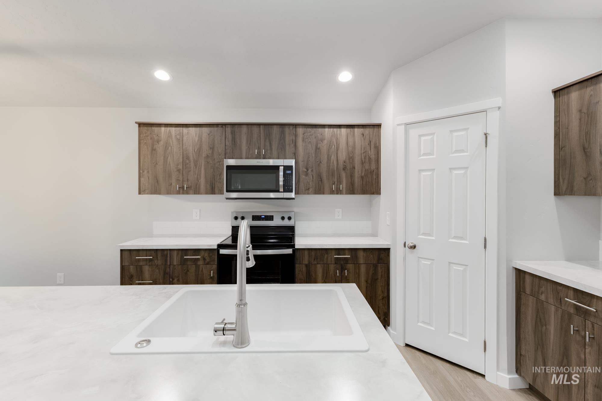Kitchen featuring modern cabinets, appliances with stainless steel finishes, light wood-style flooring, recessed lighting, and light stone countertops