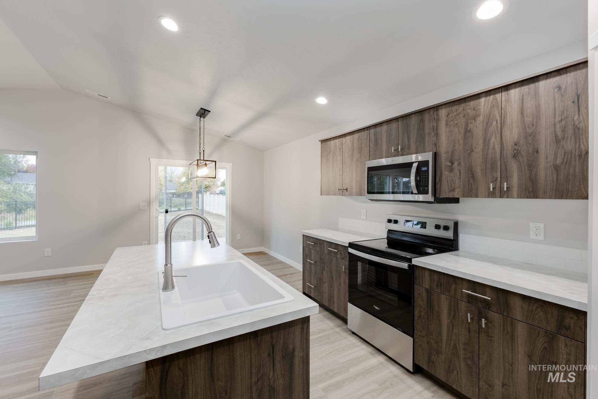 Kitchen featuring stainless steel appliances, light wood finished floors, a center island with sink, light countertops, and pendant lighting