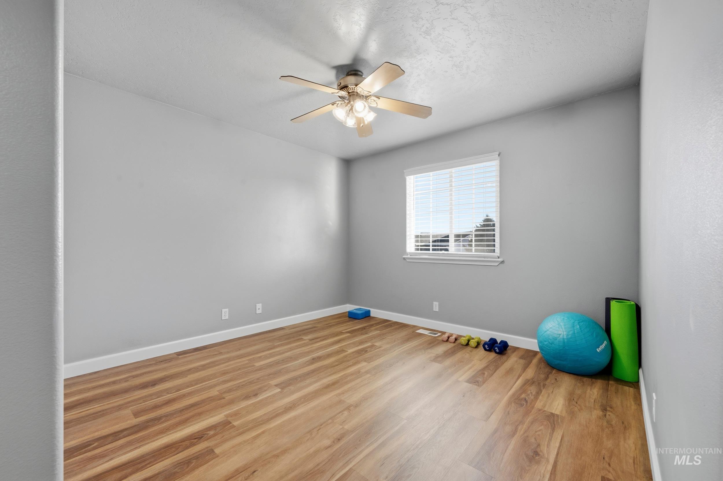 Workout area with light wood finished floors, a ceiling fan, and a textured ceiling