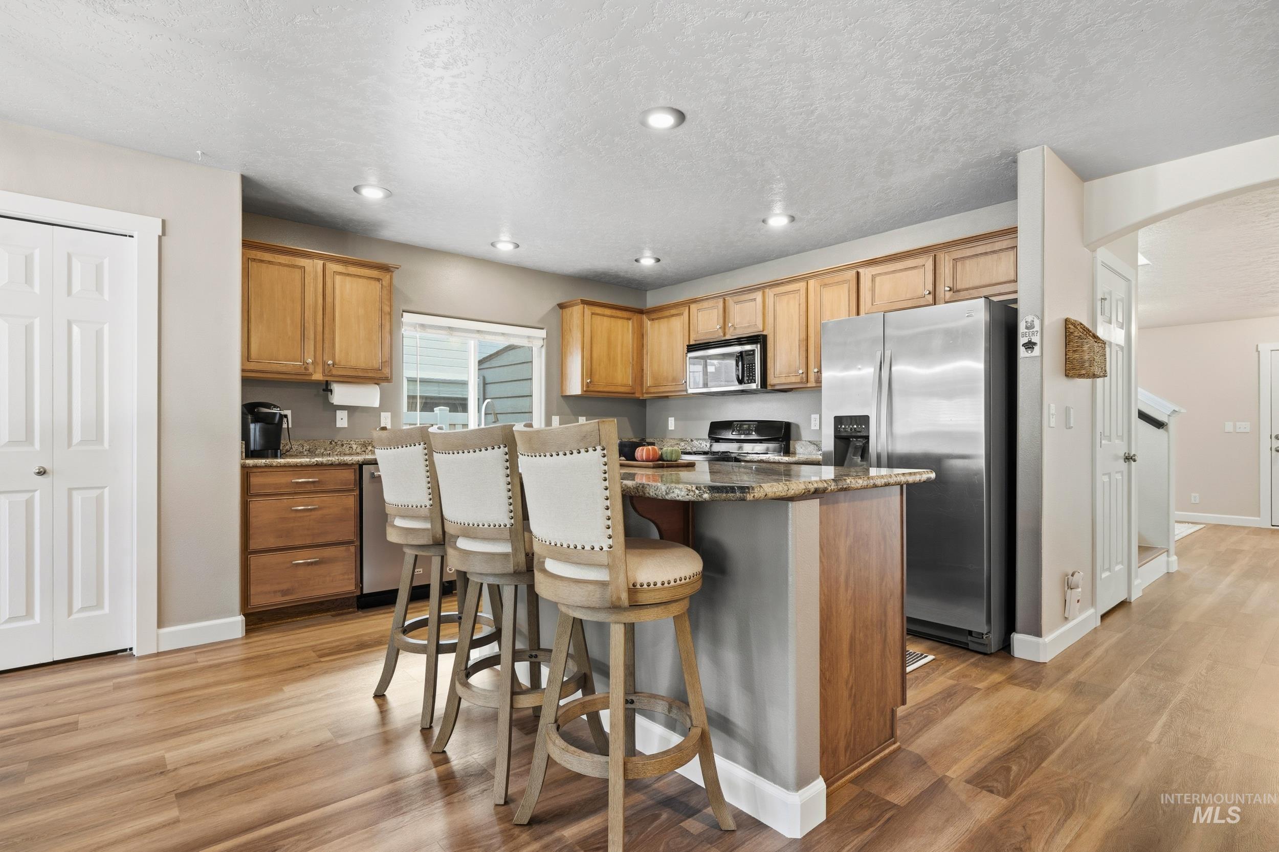 Kitchen featuring stainless steel appliances, a kitchen breakfast bar, dark stone countertops, arched walkways, and a kitchen island