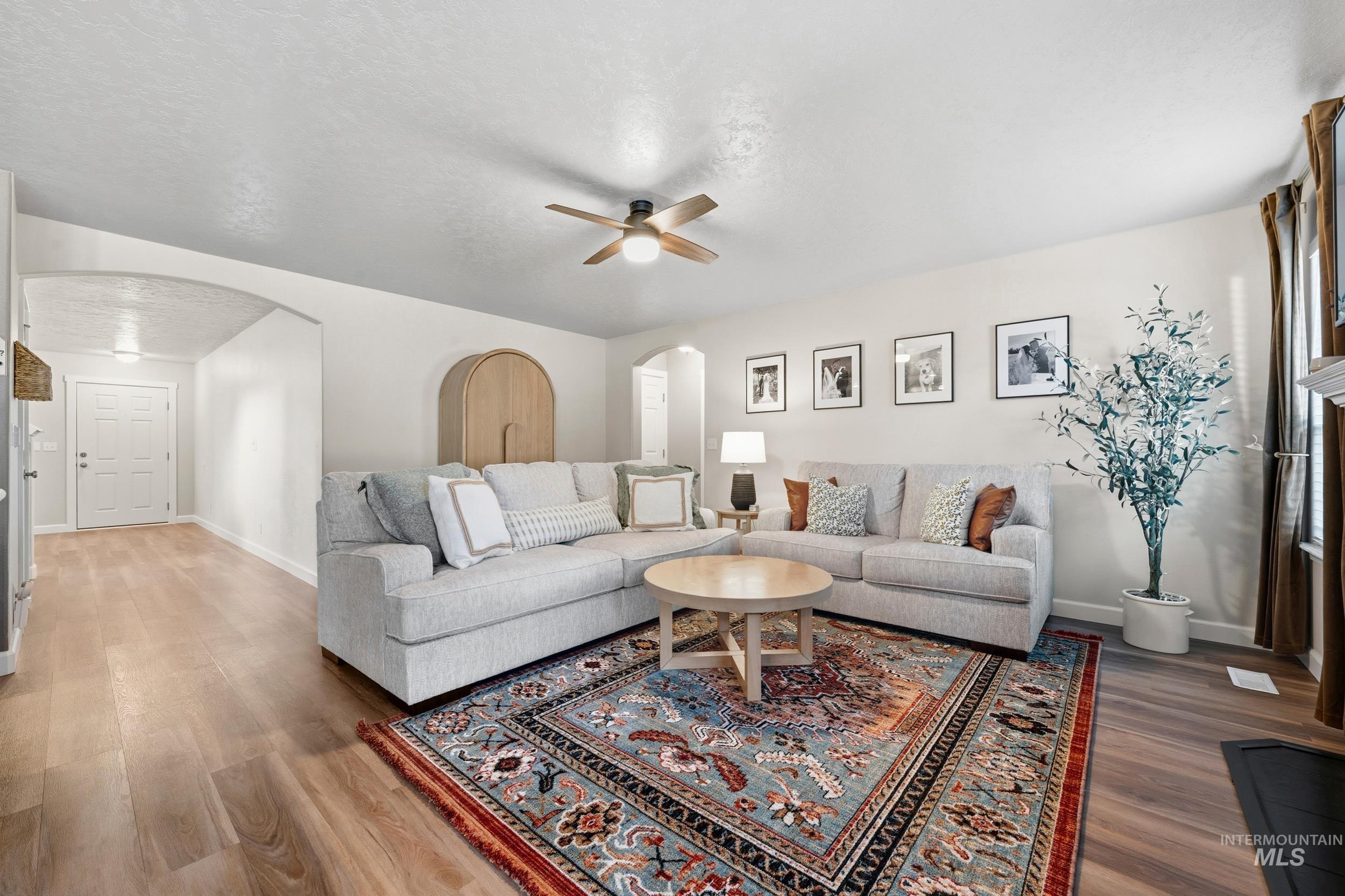 Living room with ceiling fan, wood finished floors, arched walkways, and a textured ceiling