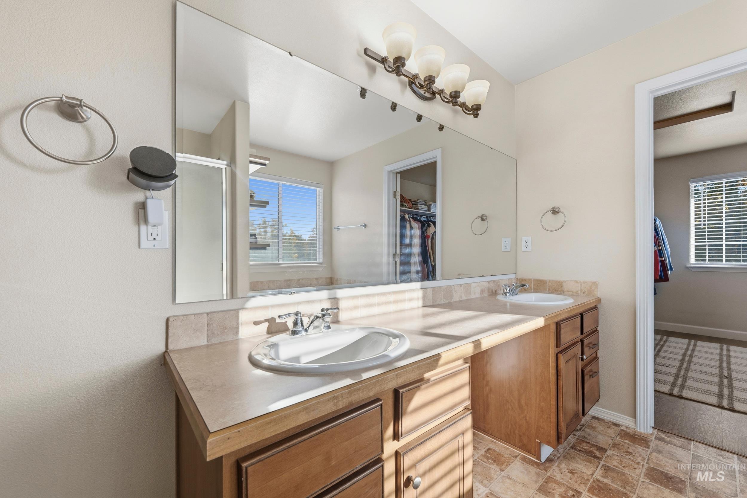 Full bathroom featuring double vanity, a shower stall, light stone finish flooring, and a walk in closet