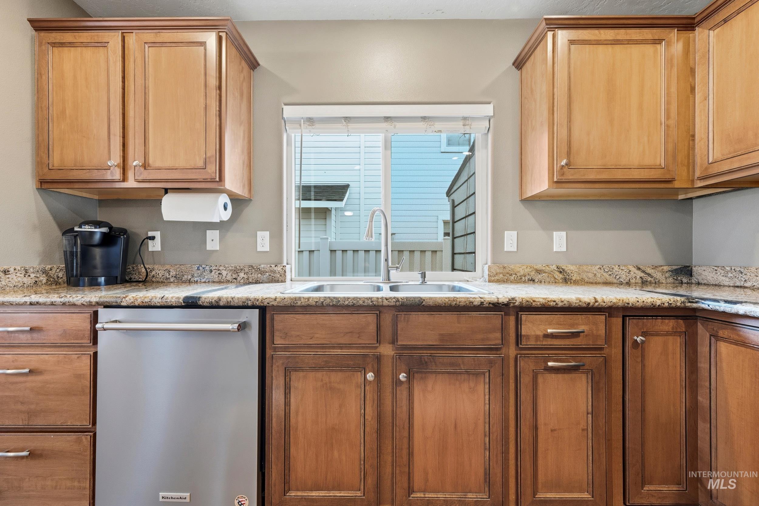 Kitchen with stainless steel dishwasher, brown cabinets, and light stone countertops
